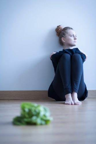 Frau mit Essstörung, sitzt nachdenklich vor Salat